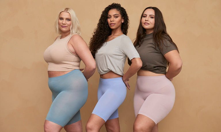 Three women modeling mid-thigh chafewear shorts in aqua, lavender, and blush with neutral tops against a beige background