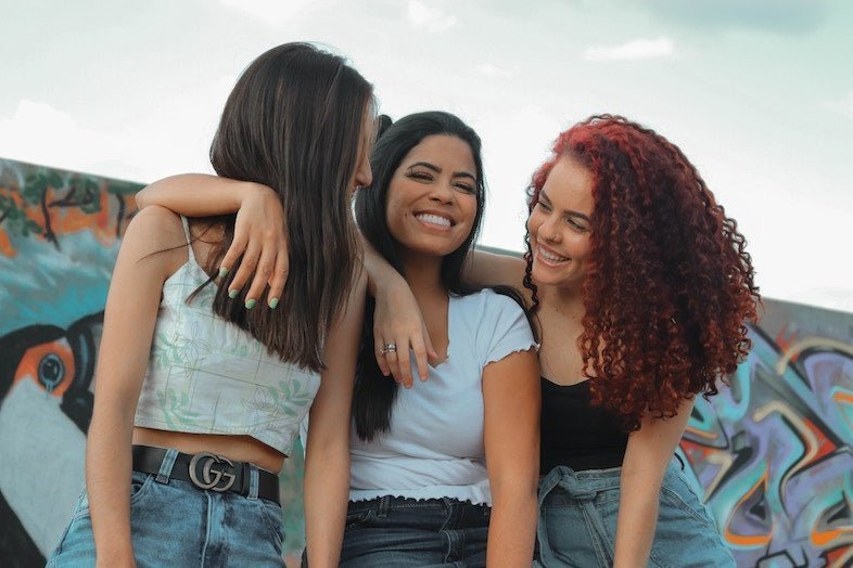 Three friends smiling in front of a colorful graffiti wall wearing fitted and cropped tops with high waisted denim