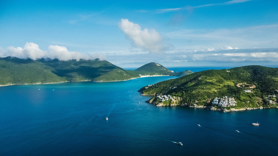 Aerial view of green islands and a turquoise bay with small boats on calm blue water under a partly cloudy sky