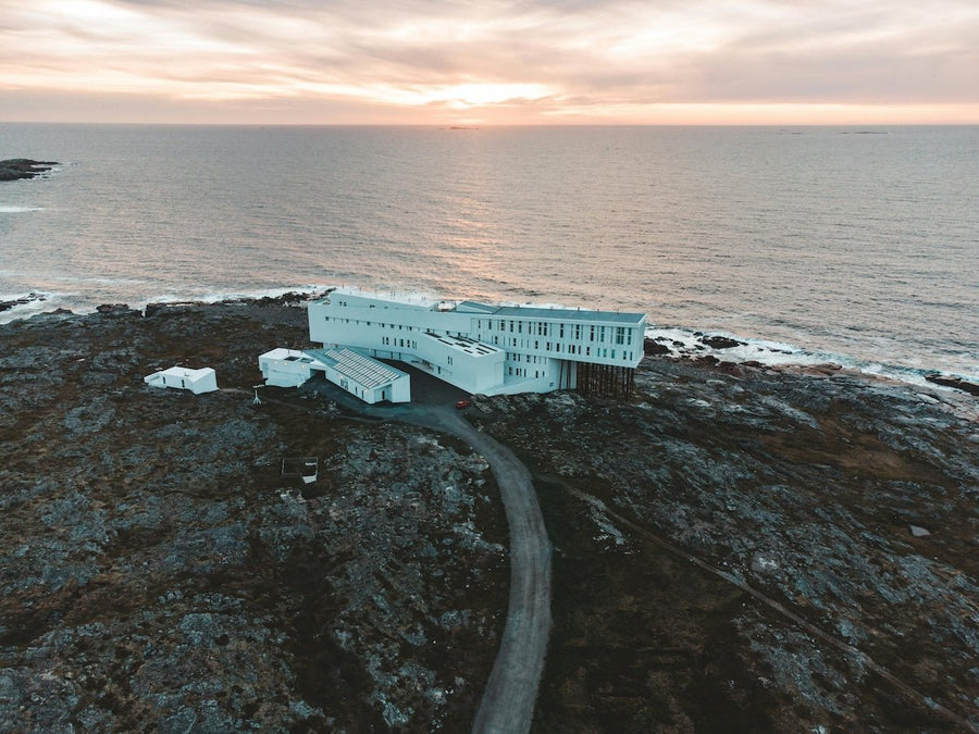 Aerial view of a modern white seaside hotel on a rocky coast at sunset