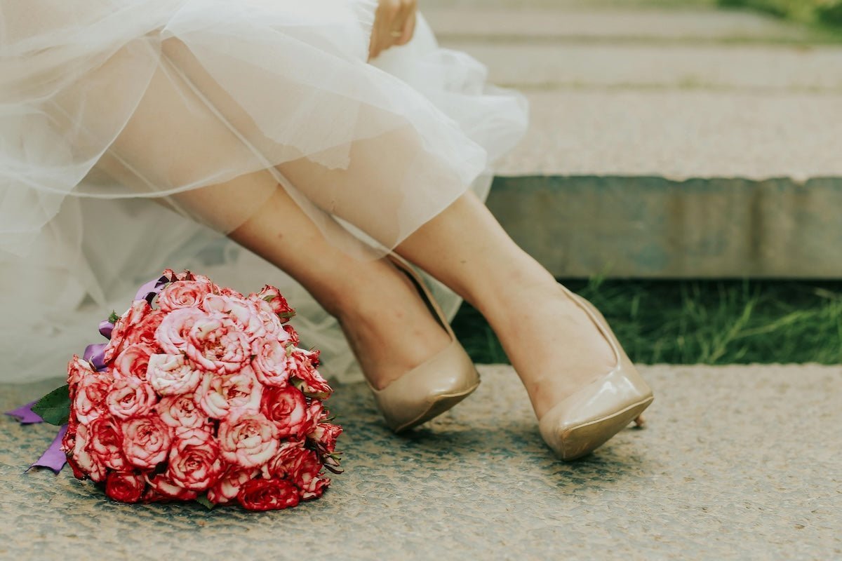 Seated bride showing tulle wedding gown and nude heels with a pink rose bouquet in the foreground