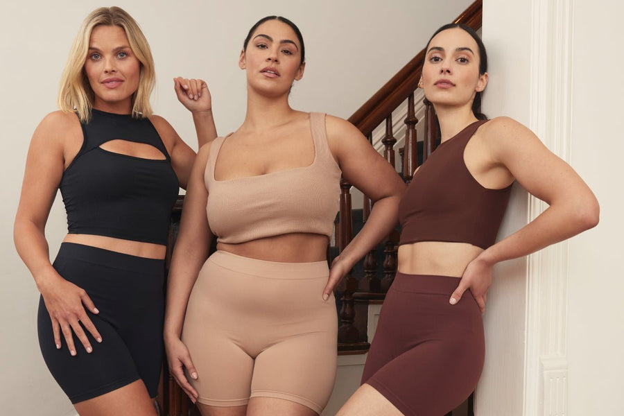 Front view of three models wearing Thigh Society shorties showing smooth mid-thigh fit in black, nude, and brown on stairs