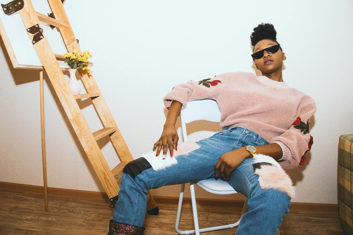 Woman reclining in a chair wearing a pink fuzzy sweater with rose embroidery and relaxed-fit jeans with fluffy knee patches