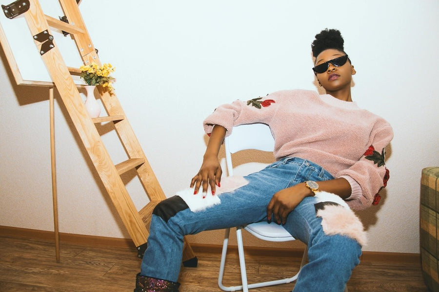 Woman reclining in a chair wearing a pink fuzzy sweater with rose embroidery and relaxed-fit jeans with fluffy knee patches