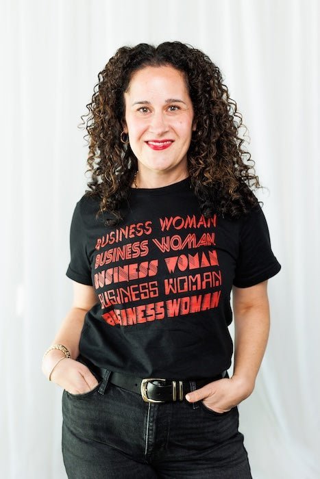Woman smiling in a black T-shirt printed with repeating red BUSINESS WOMAN text against a white backdrop