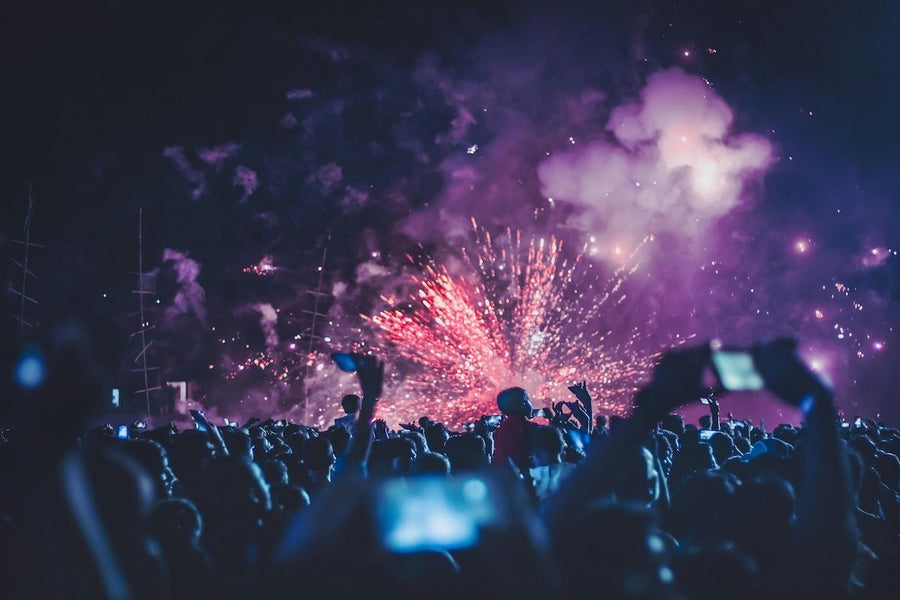 Festival crowd at night watching colorful fireworks and stage lights as people raise phones