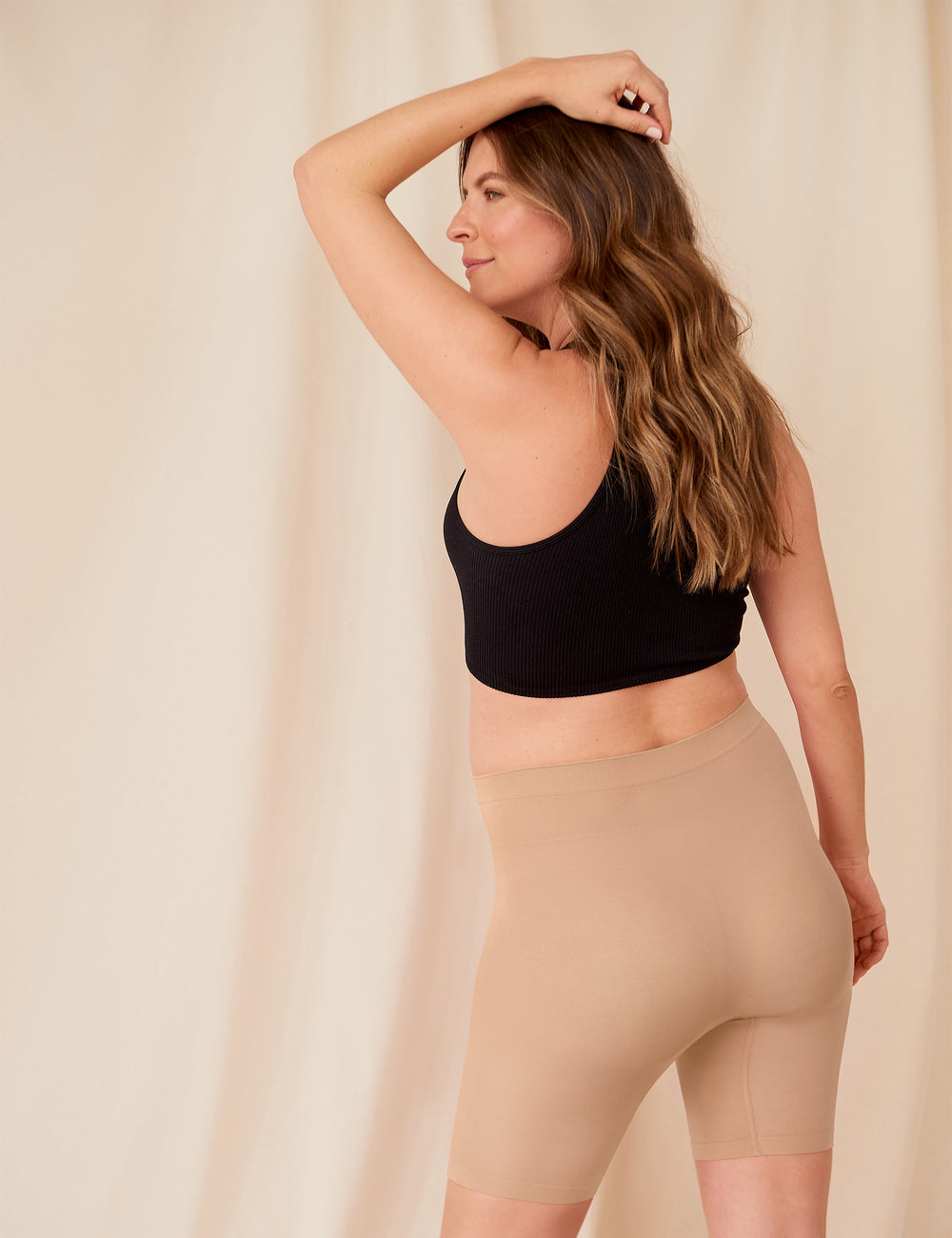 Back view of The Staple maternity 5-inch shorts in almond showcasing anti-chafe fabric and high waist on model with beige backdrop