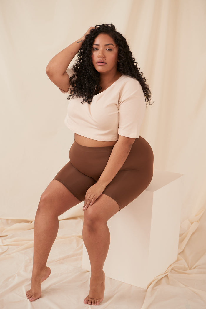 Seated view of Cooling 7-inch anti-chafe shorts in cocoa showing high waist and smooth fit on model against cream backdrop