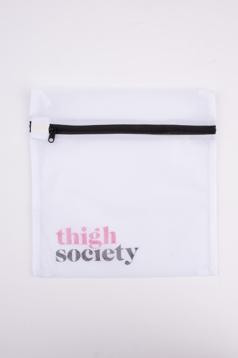 Top-down view of white mesh delicates wash bag with black zipper and pink and gray thigh society logo on white background